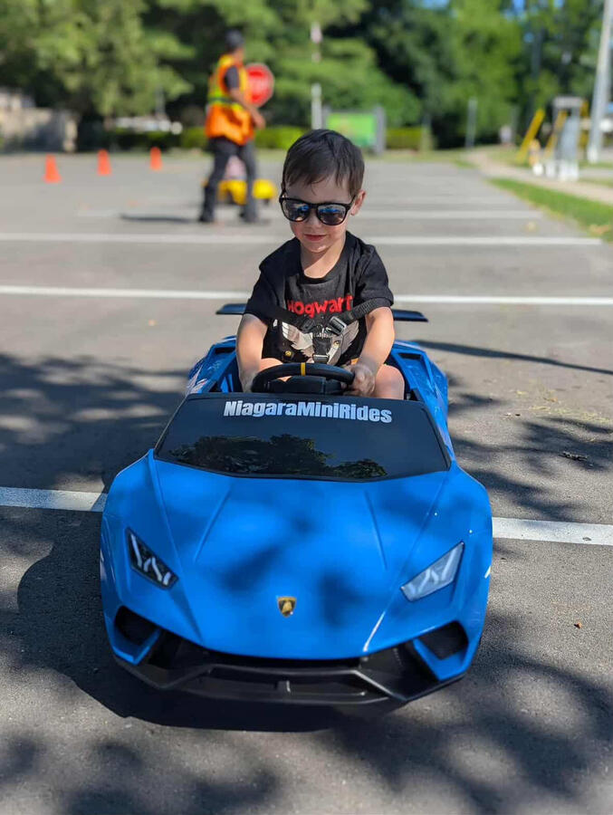 Kids love the Mini Lambo Experience. Safe, stylish, and unforgettable fun. Child driving blue and yellow Lamborghini ride-on cars at outdoor kids party.
